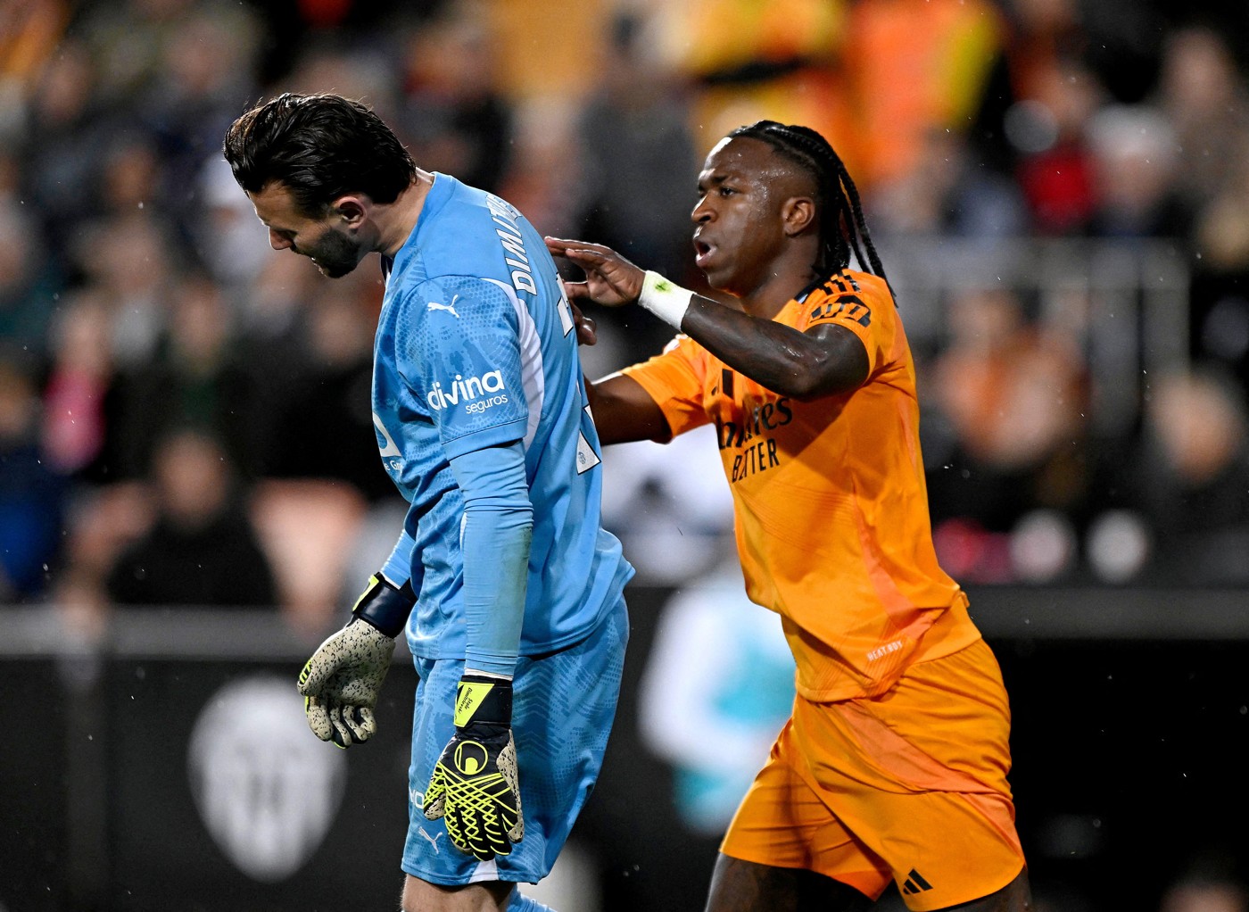 Vinícius, con equipación naranja, coloca las manos sobre la nuca de Dimitrievski, con camiseta azul, en Mestalla el 3 de enero de 2025.